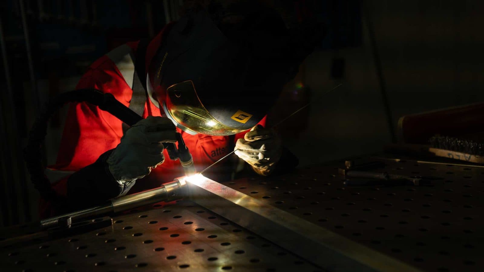 TIG-sveising av aluminiumsprofil til en sperreport, med lysbuen som eneste lyskilde i verkstedet