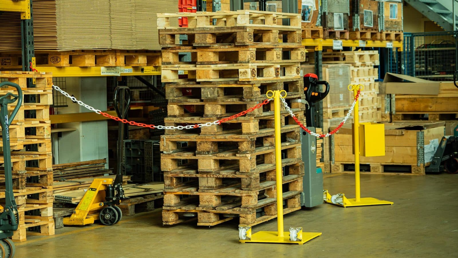 Rød/hvit kjetting spent mellom to sperrevogner foran en pallestabel i lagerhall