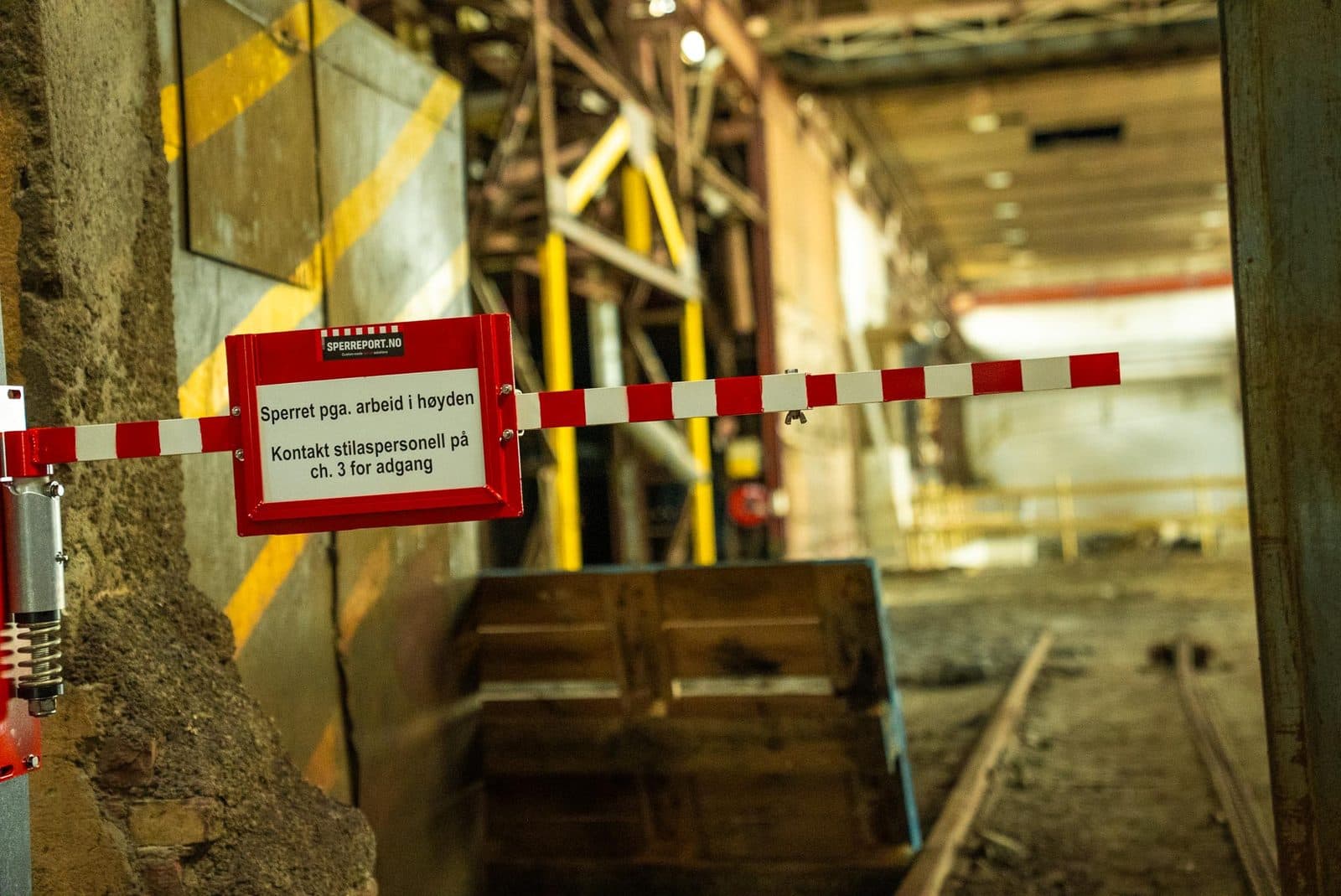 Sperreport sperrer av en passasje i industrihallen, med rødt HMS-skilt i skiltholderen