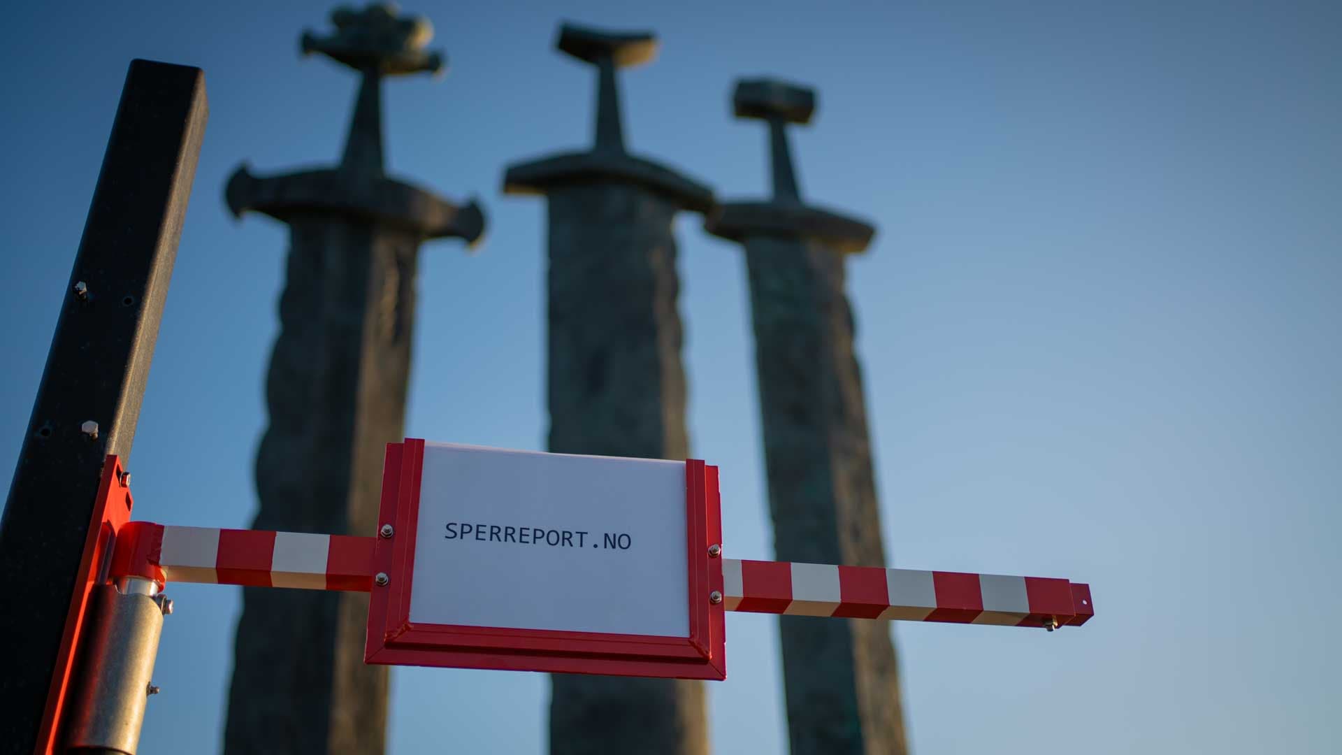 A Sperreport safety barrier gate seen from the side, with a red/white telescopic arm and integrated sign holder, mounted outdoors in front of Sverd i fjell in Hafrsfjord
