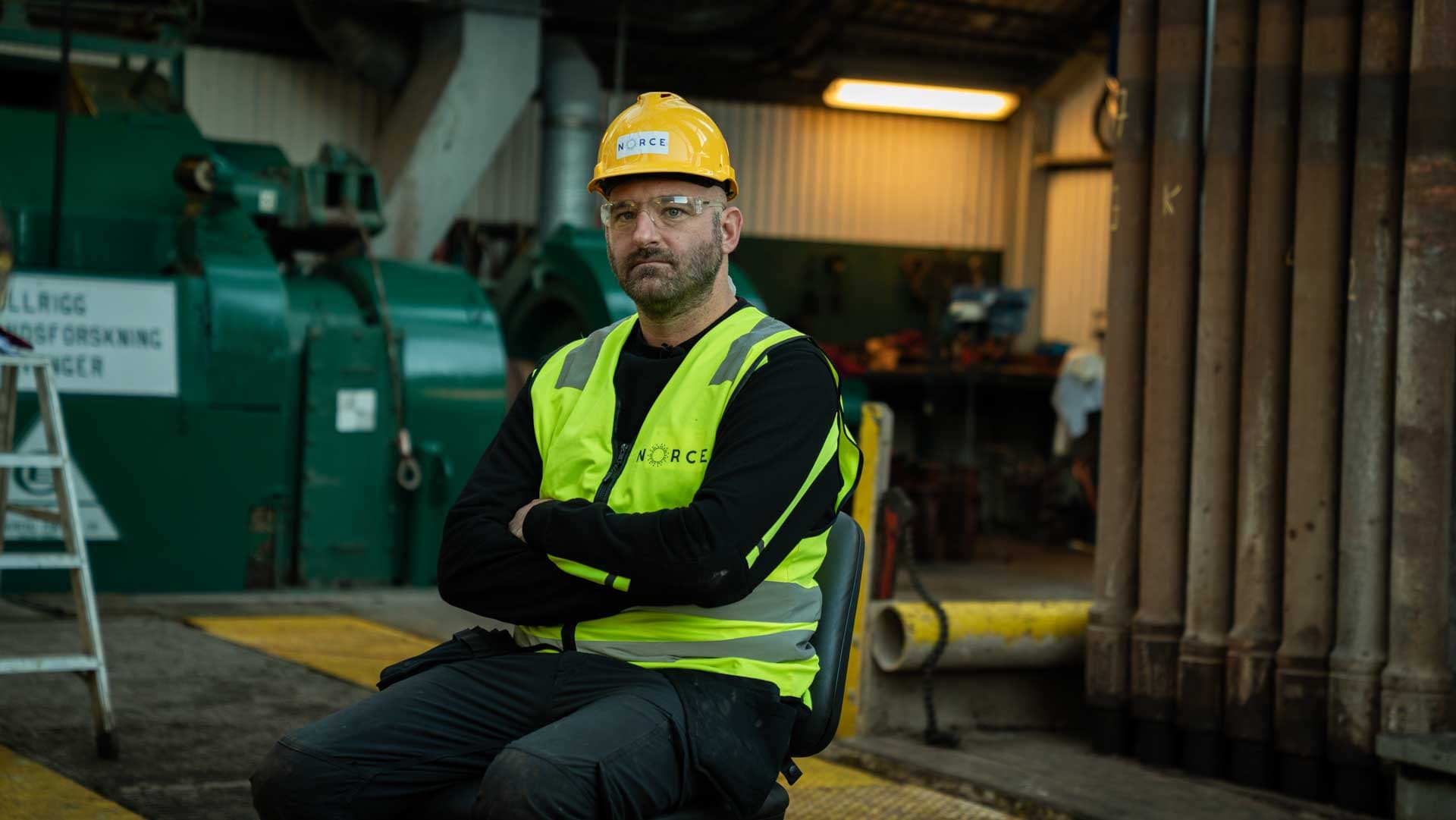 Industriarbeider med NORCE-vernevest og hjelm i verkstedhall på Ullrigg, Canrig-utstyr i bakgrunnen